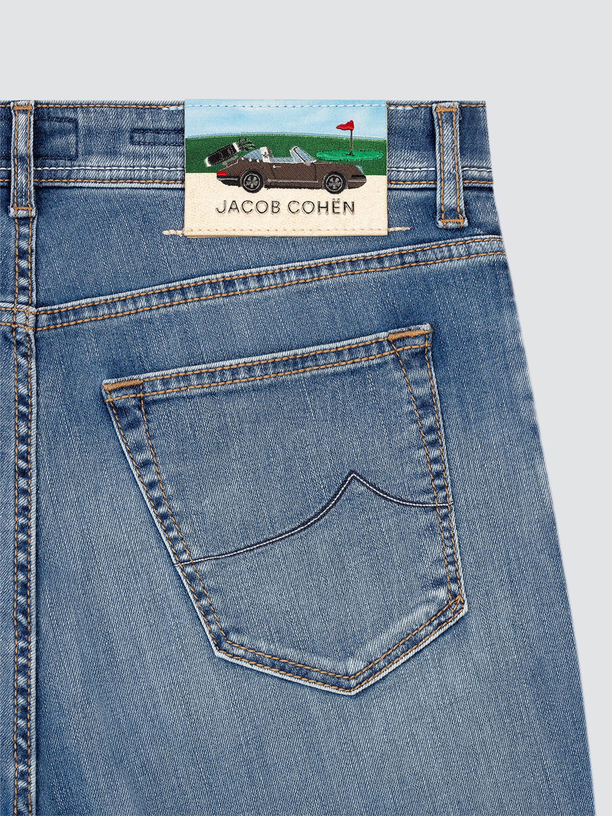 Close-up of blue jeans with a Jacob Cohen label GOLF AND PORSCHE on a light gray background
