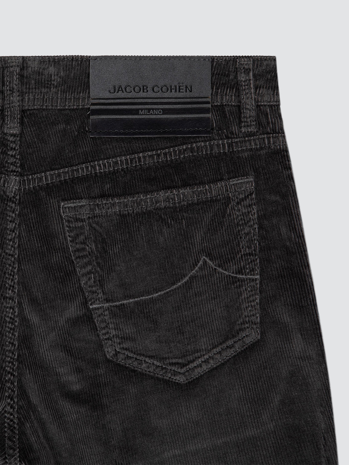 Close-up of the back waistband and pocket of black corduroy jeans by Jacob Cohen, showing the brand label and fabric texture against a light gray background.