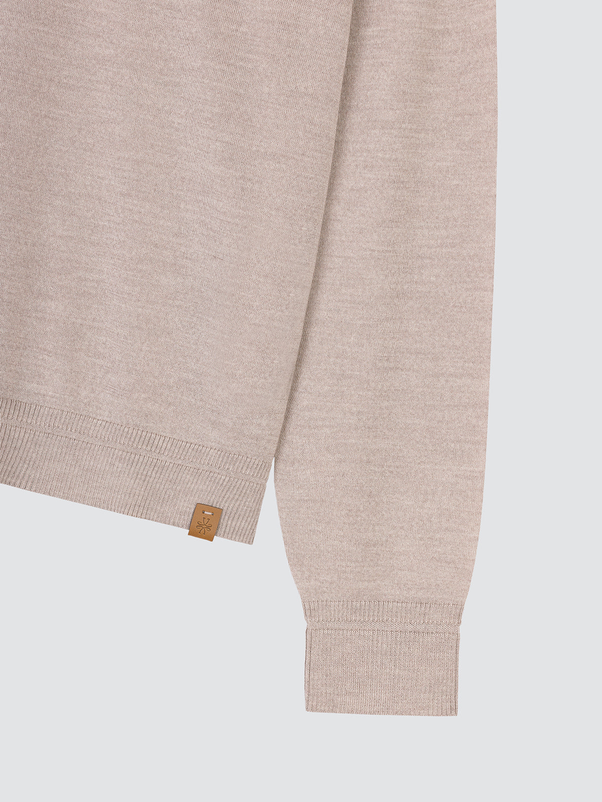 Close-up of the ribbed cuff and leather logo tab of the light greige polo