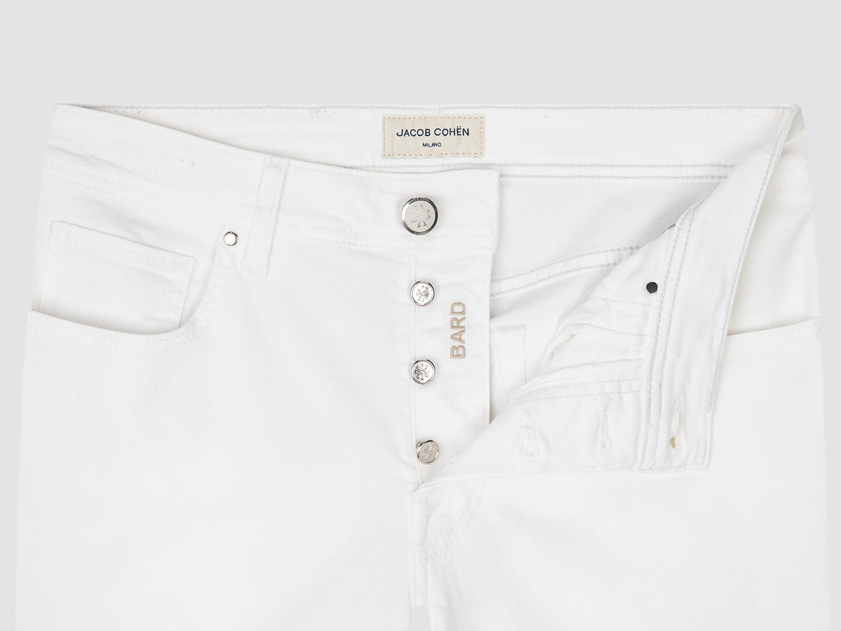 Close-up of white TWILL jeans showing the waistband, button closure, pocket, and a small gold-tone embroidered BARD logo on the side.