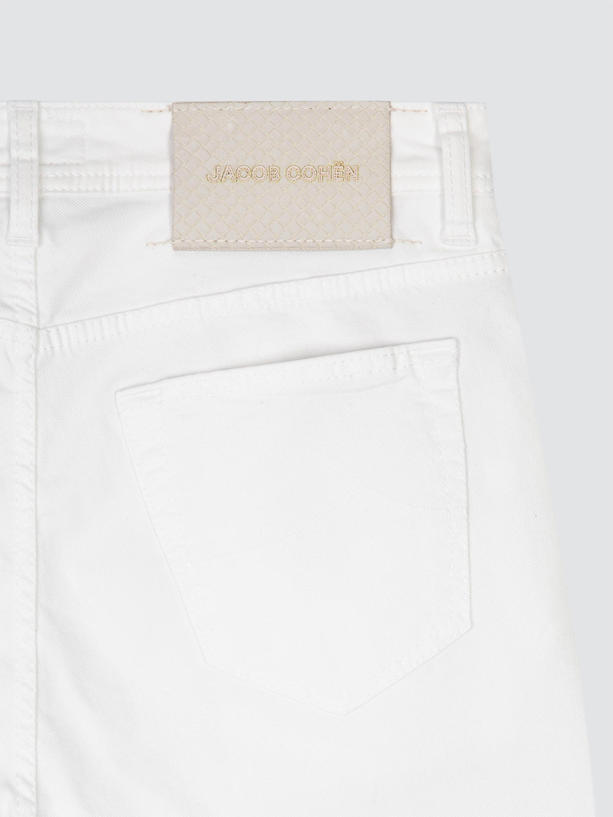 Close-up of white denim jeans showing the back waistband with a beige JACOB COHEN brand patch and a back pocket, on a light gray background.