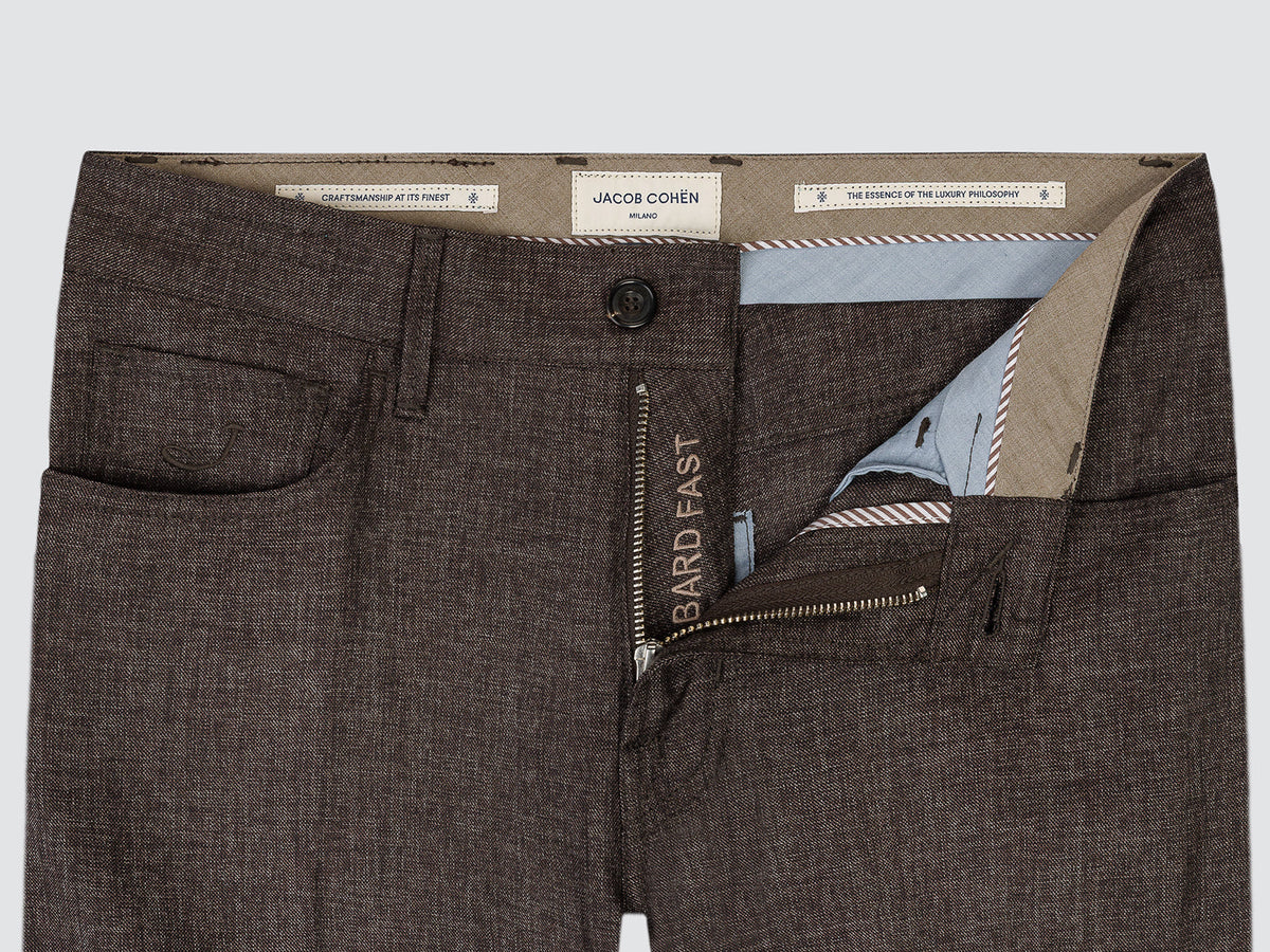 Close-up of the open waistband of the brown wool trousers, showing the horn tack button, the contrast inner facing and the branded interior tab.