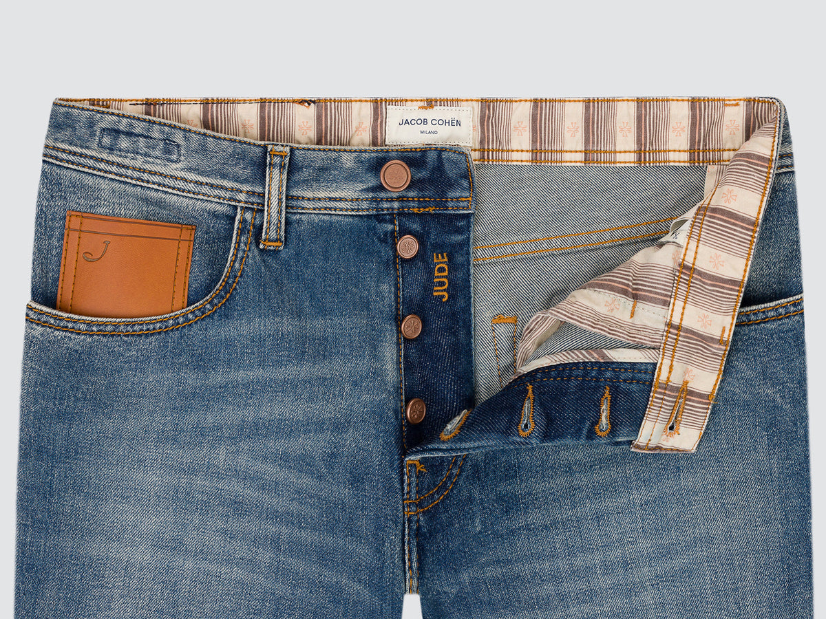 Close-up of the open button fly of the Jude jeans, showing the copper-finish button, the leather waistband patch and the striped inner facing.
