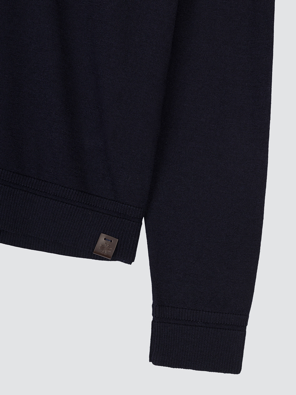 Close-up of the ribbed cuff and leather logo tab of the navy polo