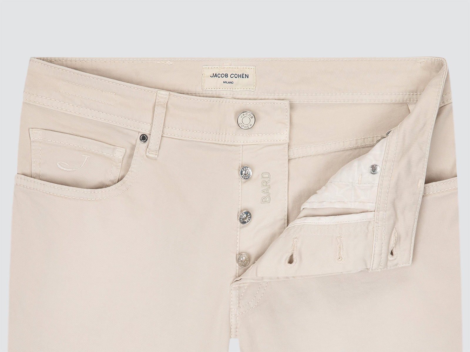 Close-up of a pair of light beige denim jeans by Jacob Cohen, showing the waistband, front button closure, and side pockets on a light gray background.