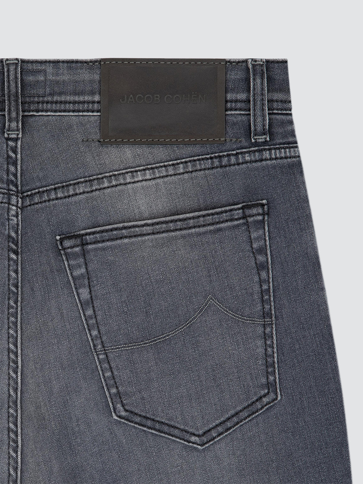 Close-up of the back waistband and pocket of dark gray denim jeans, showing a dark grey leather patch with the brand name JACOB COHEN