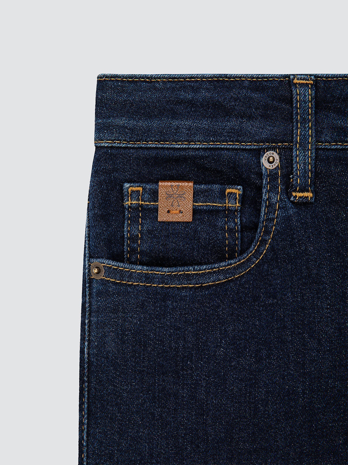 Close-up of dark blue jeans with a brand logo Jacob Cohën on the pocket against a light gray background