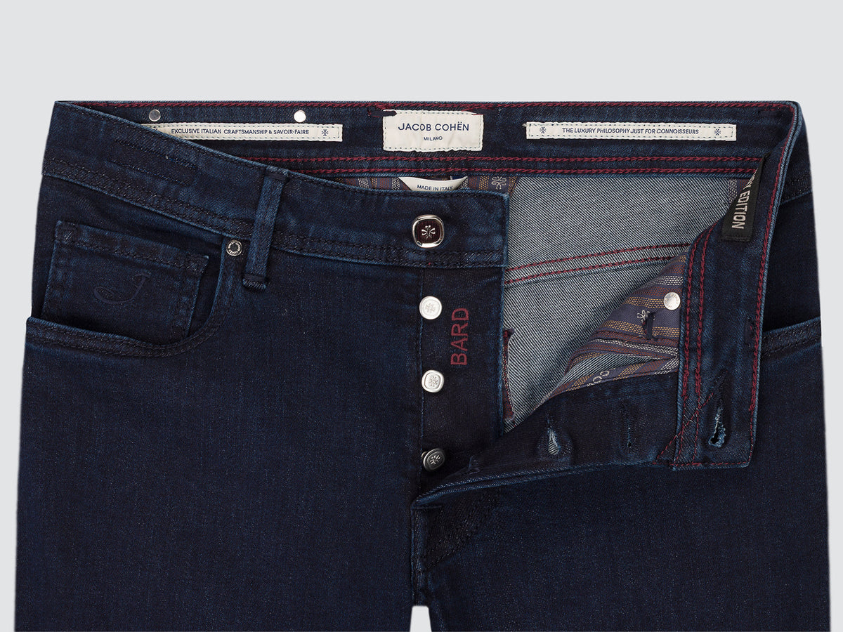 Close-up of the open button fly of dark blue Bard jeans, showing the squared steel button, the grey inner facing and the Jacob Cohën interior tabs.