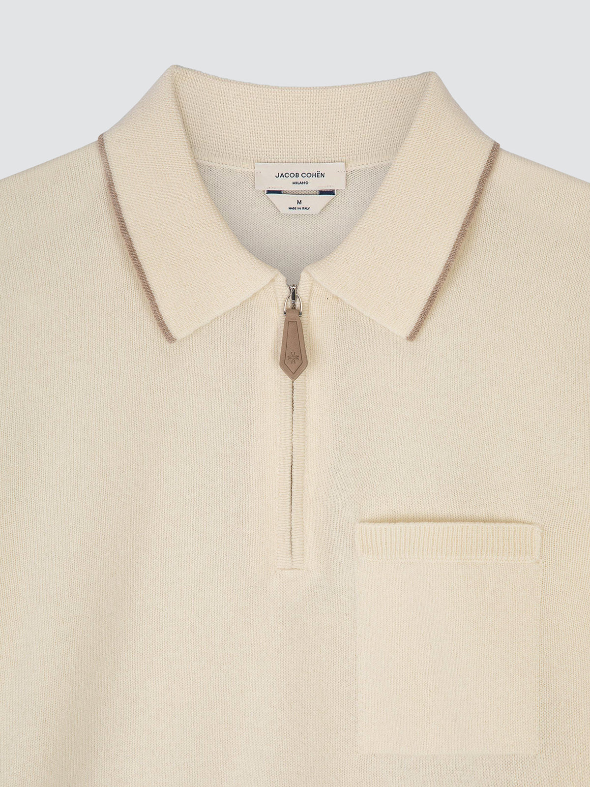 Close-up of the knitted collar, half-zip fastening and patch chest pocket of a cream cashmere Jacob Cohën polo, with the brand label at the neck.