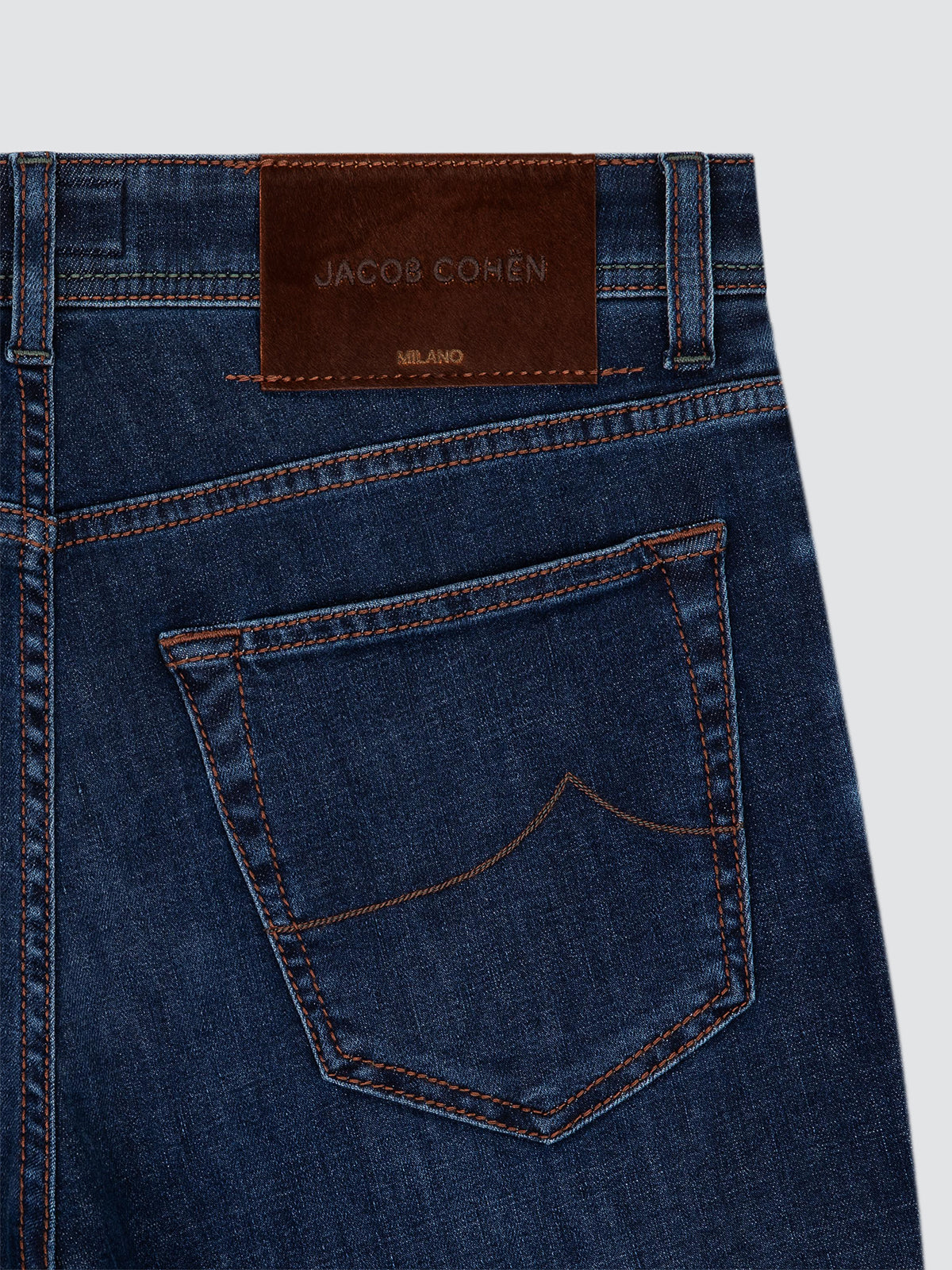 Close-up of the back waistband and pocket of dark blue denim jeans with a brown leather patch showing the JACOB COHEN brand.