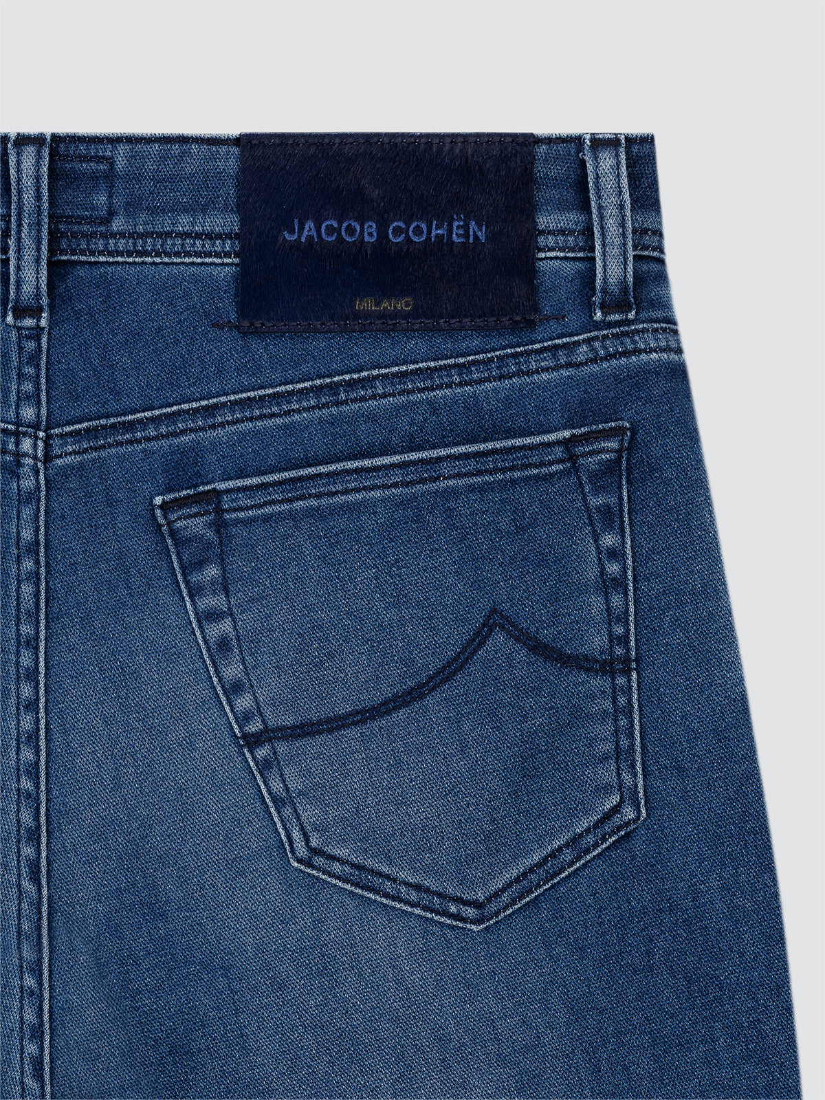 Close-up of blue denim jeans with Jacob Cohen label on a light gray background