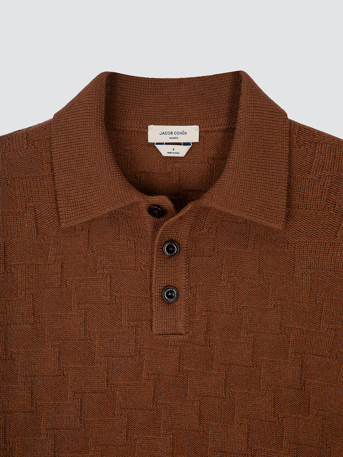 Close-up of a brown textured knit polo shirt in wool and cashmere, showing the classic collar, the horn button placket and the houndstooth stitch.