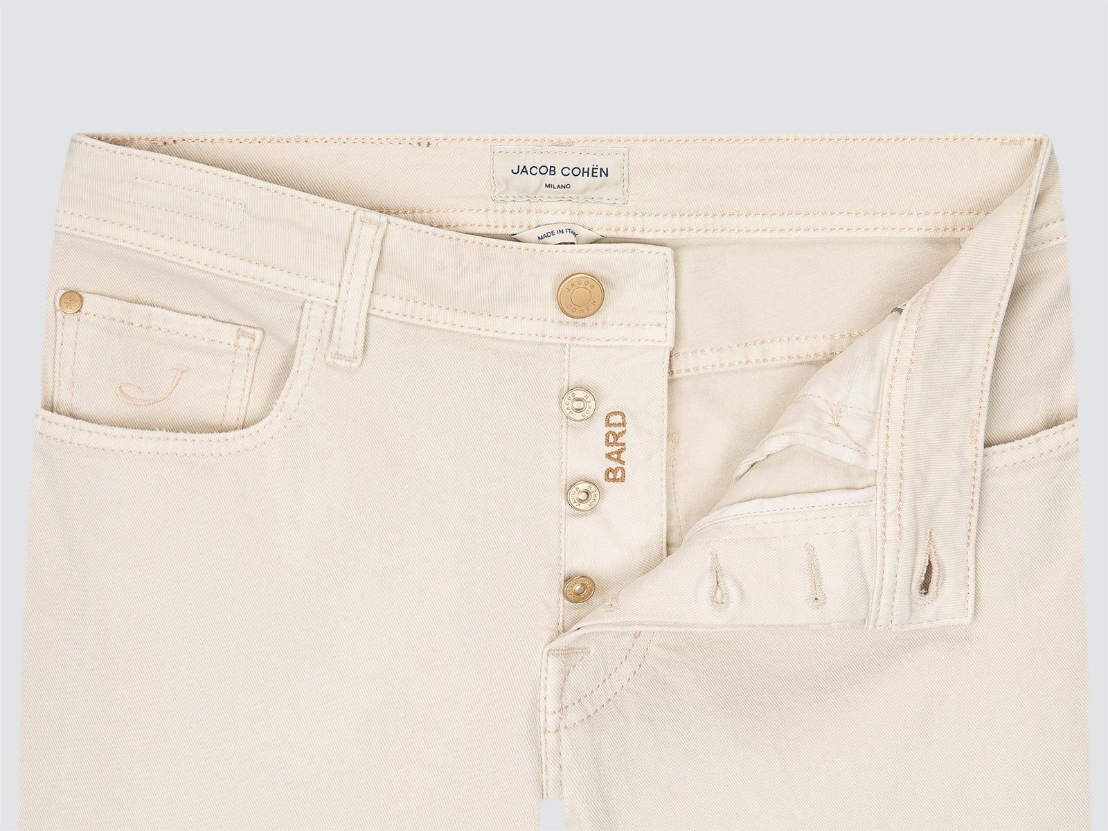 Close-up of a pair of light cream denim jeans by Jacob Cohen, showing the front button fly, gold-tone buttons, and the BARD logo on the button placket.