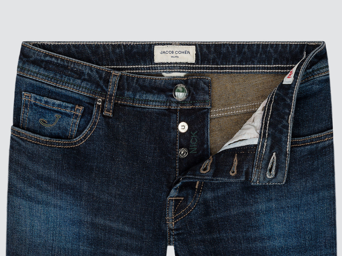 Close-up of the open button fly of blue Nick jeans, showing the enamelled tack button, the belt loops and the light inner facing.