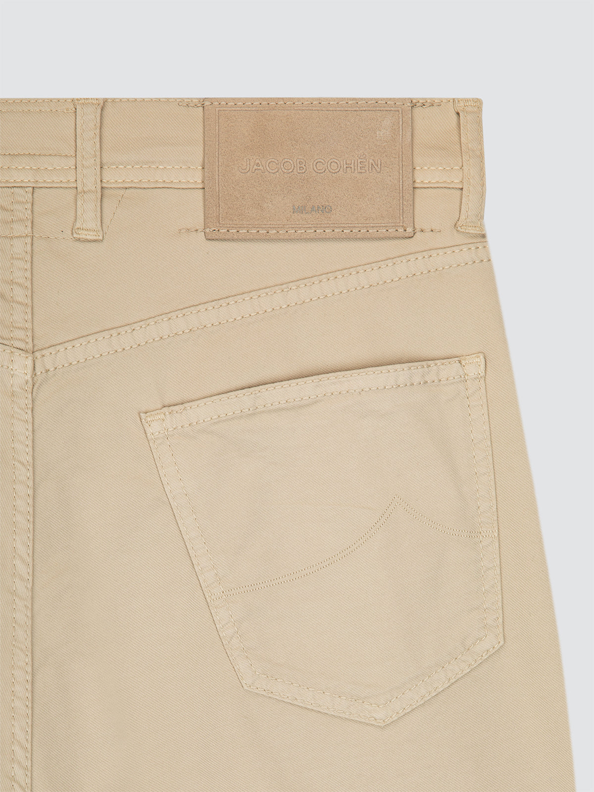 Close-up of beige short with a pocket and brand label Jacob Cohën on a light gray background