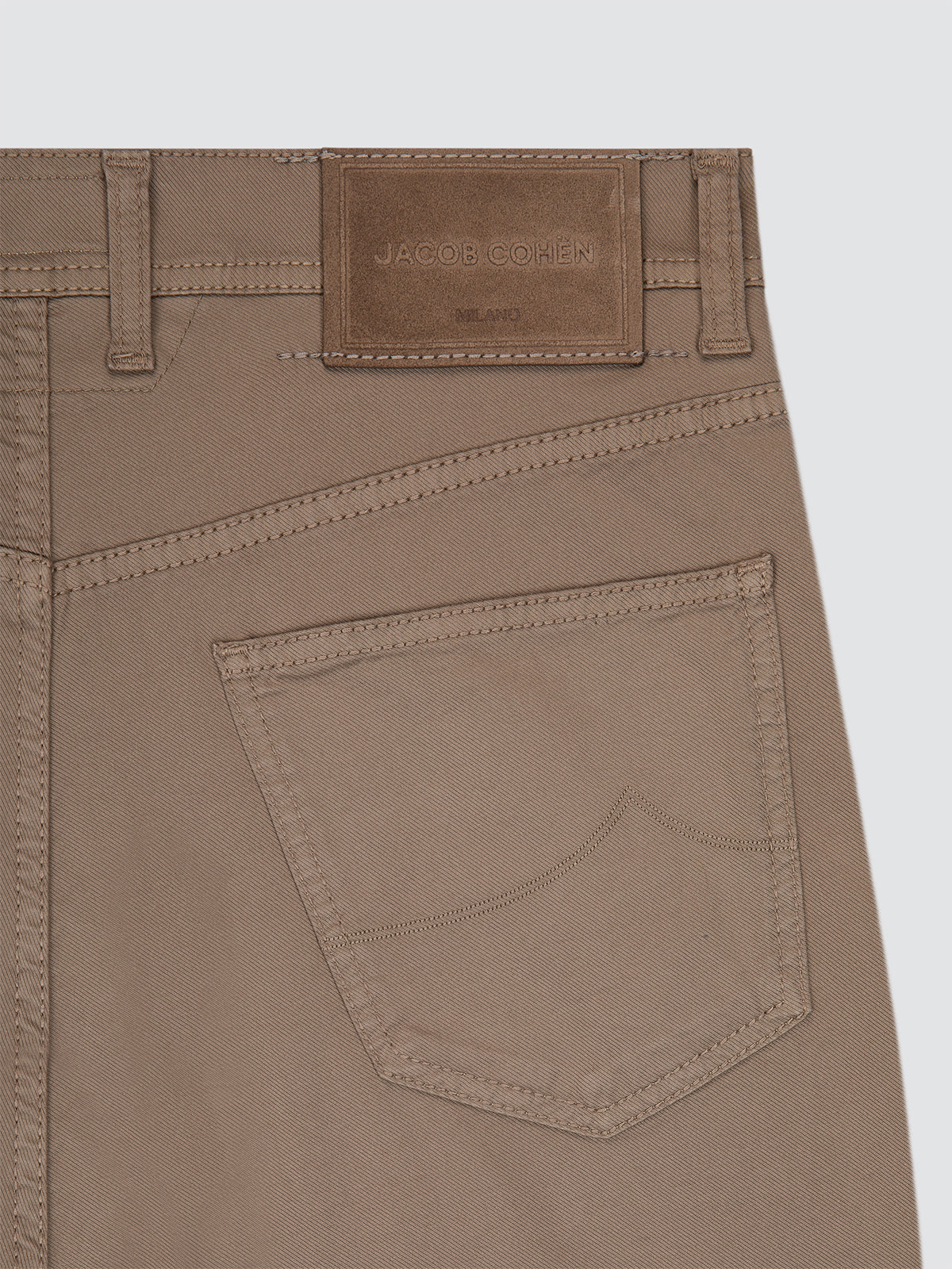Close-up of brown pants with a brand label on a light gray background