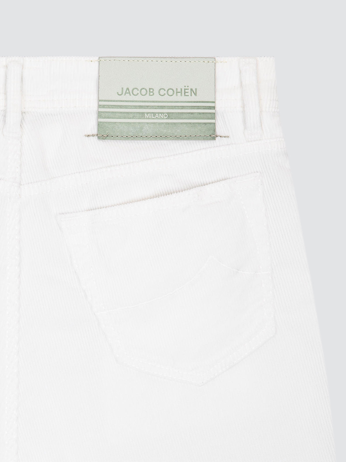 Close-up of the back waistband of white corduroy jeans by Jacob Cohën, showing the brand label and a back pocket against a light gray background.