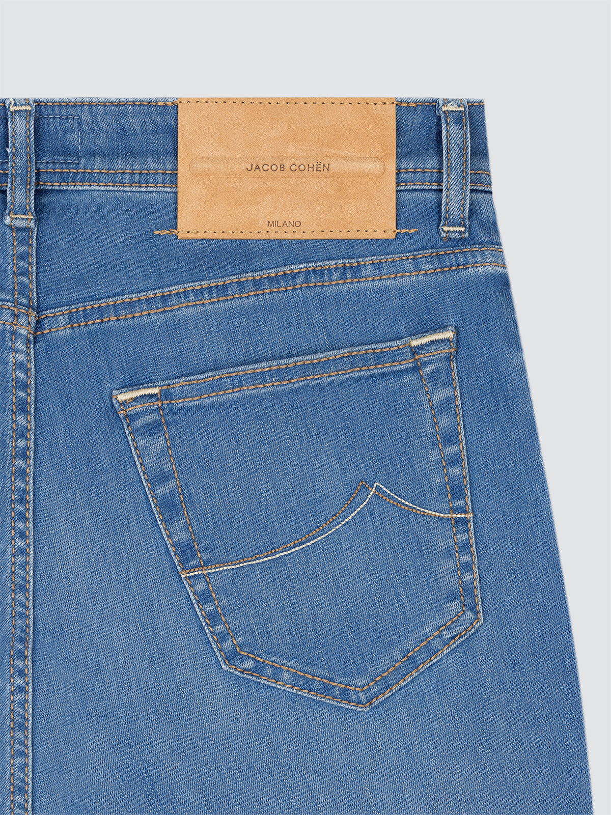 Close-up of blue jeans with a beige patch brand label on a light gray background