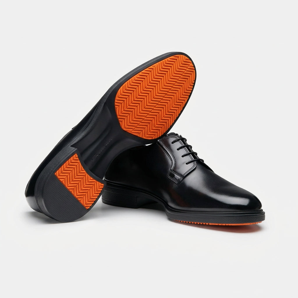 A pair of men's black leather lace-up dress shoes, with one shoe turned to show the textured orange outsole against a clean white background.