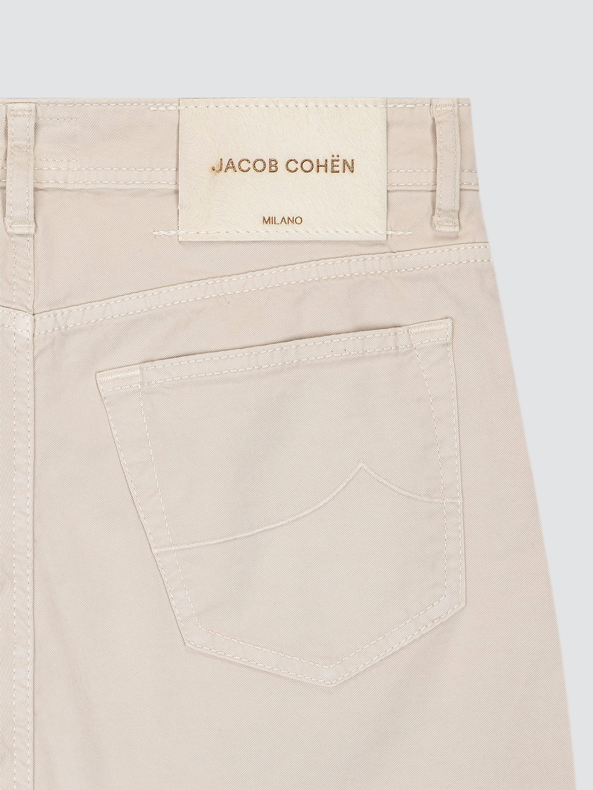 Close-up of the back waistband and pocket of light beige denim jeans, showing the JACOB COHËN MILANO label.
