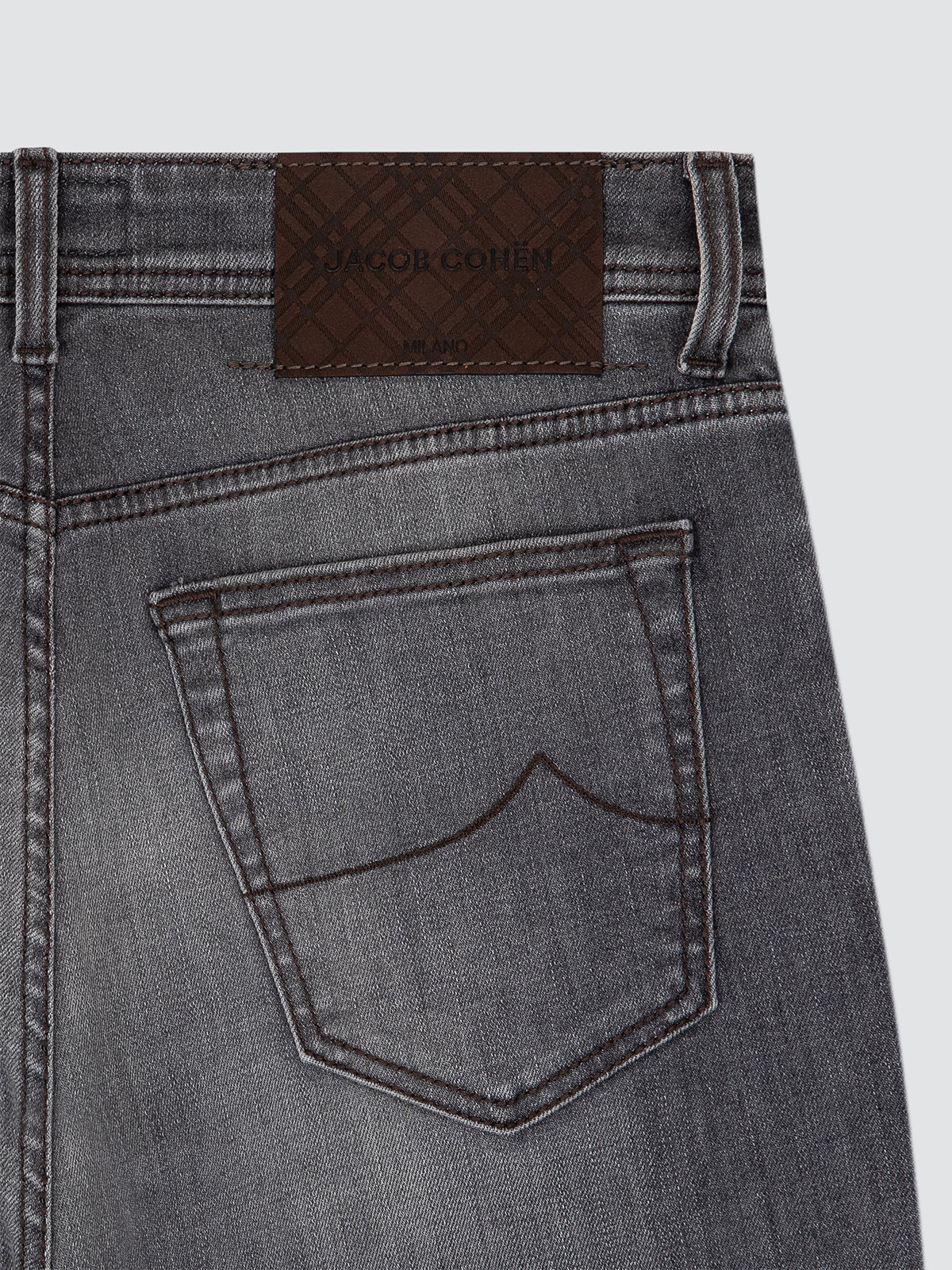 Close-up of the back waistband and pocket of gray denim jeans, showing a brown Gucci leather patch with the brand name.