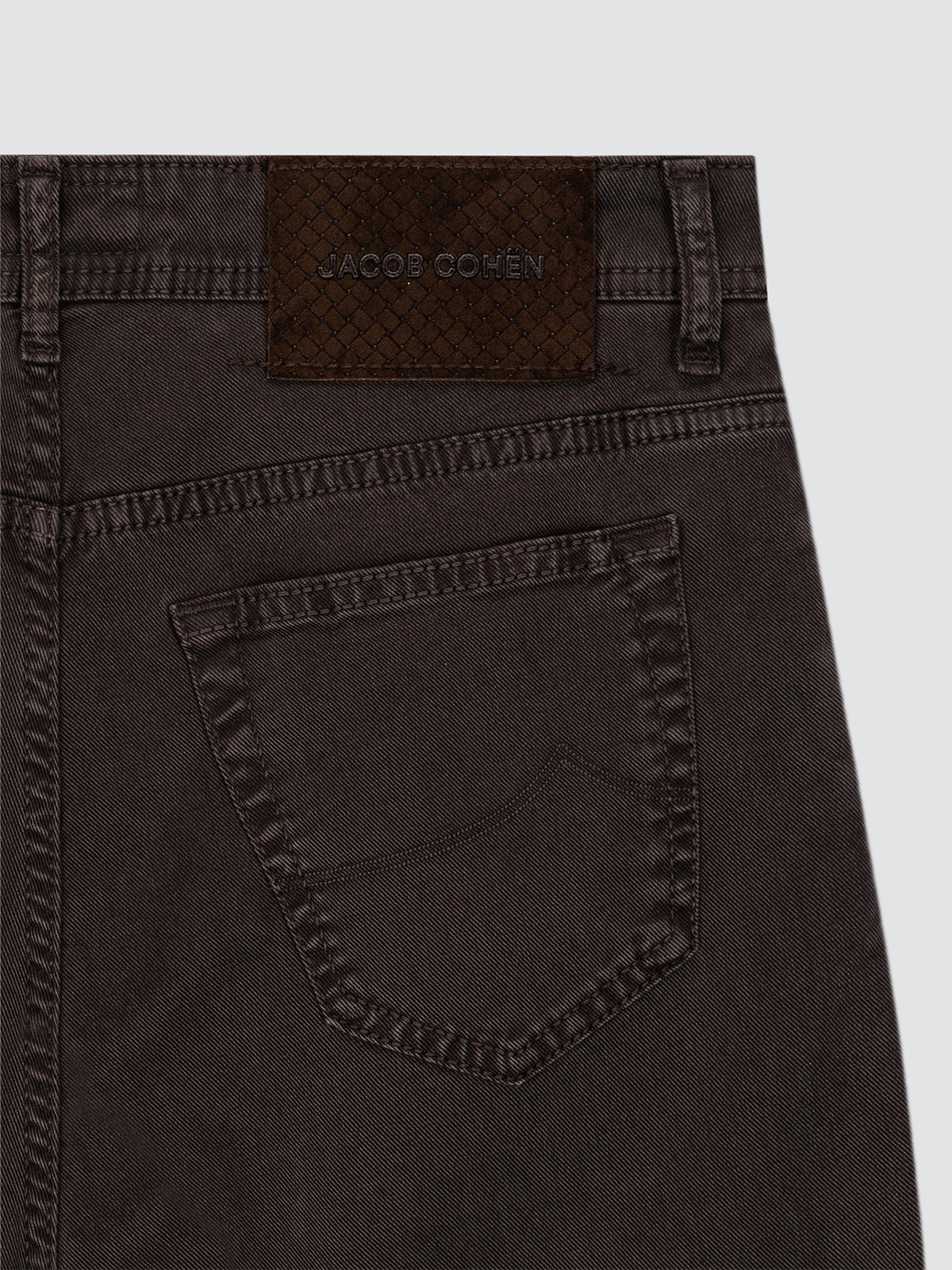Close-up of the back waistband and pocket of dark brown washed denim jeans, showing a woven Jacob Cohen brand patch.