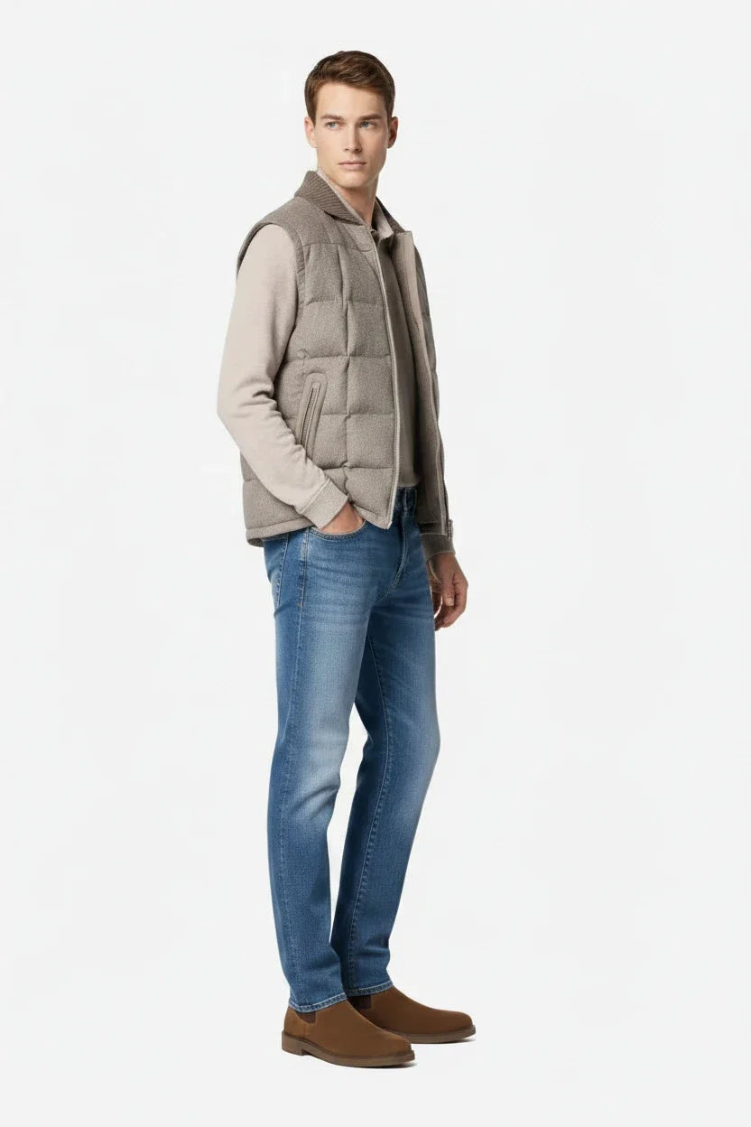Man wearing a gray vest over a shirt with blue jeans and brown shoes on a white background